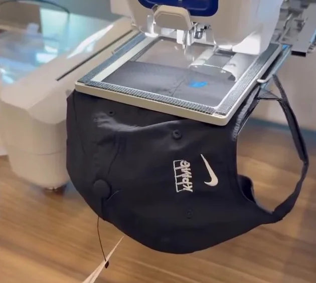 A black cap held beneath an embroidery machine at a conference
