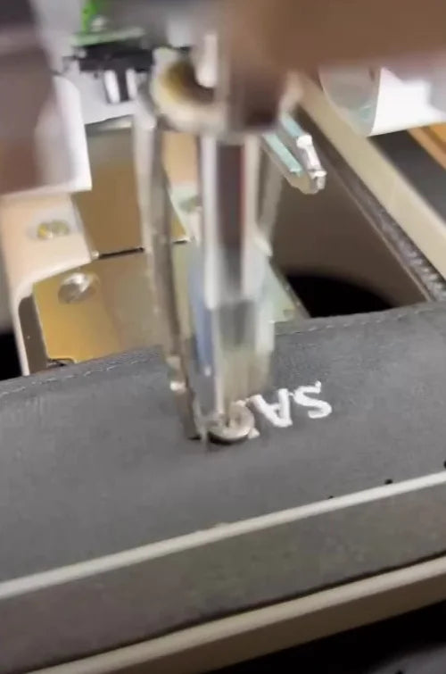 Small white lettering being embroidered onto dark golf headwear