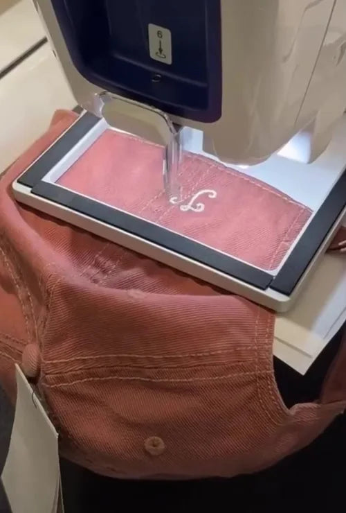 A white monogram being embroidered onto pink denim