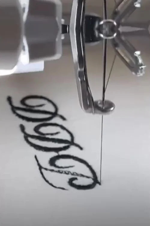 An embroidery machine stitching a black script monogram onto a white pajama top