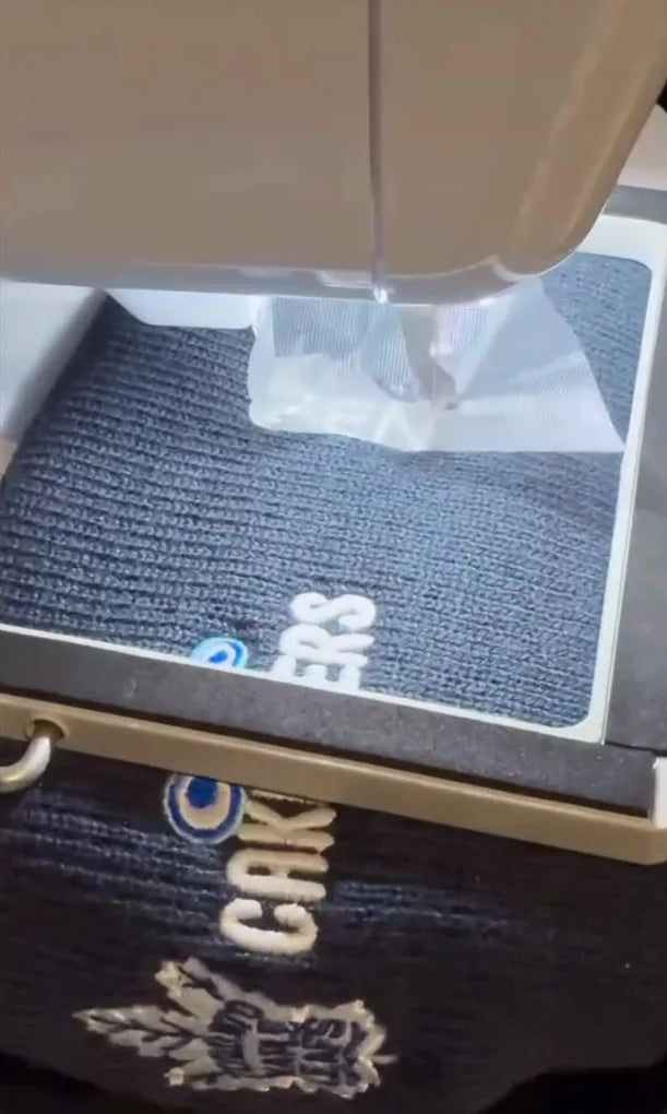 An embroidery machine stitching a dark knit toque