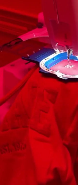 An embroidery machine stitching a pink bag under event lighting