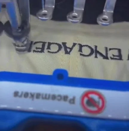 Multi-needle embroidery machine stitching dark lettering on light fabric in a blue hoop.