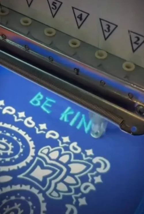 Embroidery machine adding BE KIND lettering to a blue patterned bandana.