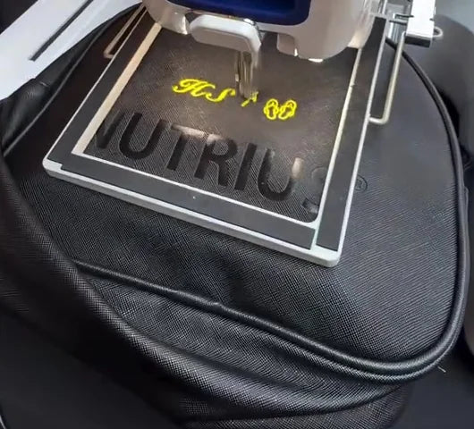Dark Nutrius zippered bag in an embroidery hoop with bright yellow stitching.