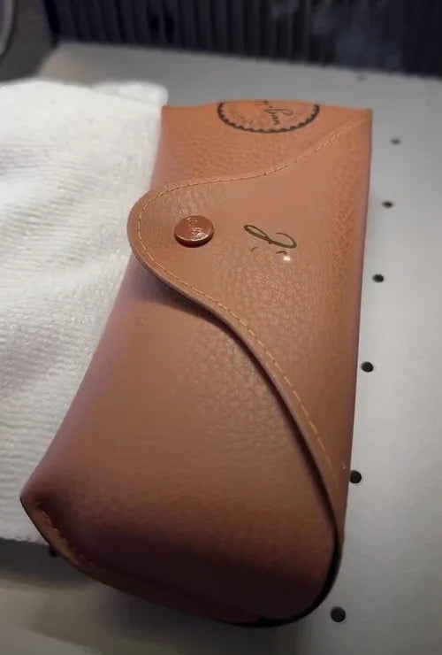 Brown Ray-Ban glasses case during laser engraving, with a small unfinished mark on its flap.