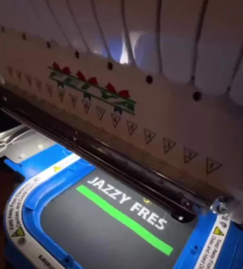 Embroidery machine stitching the nickname JAZZY FRES onto dark event apparel.