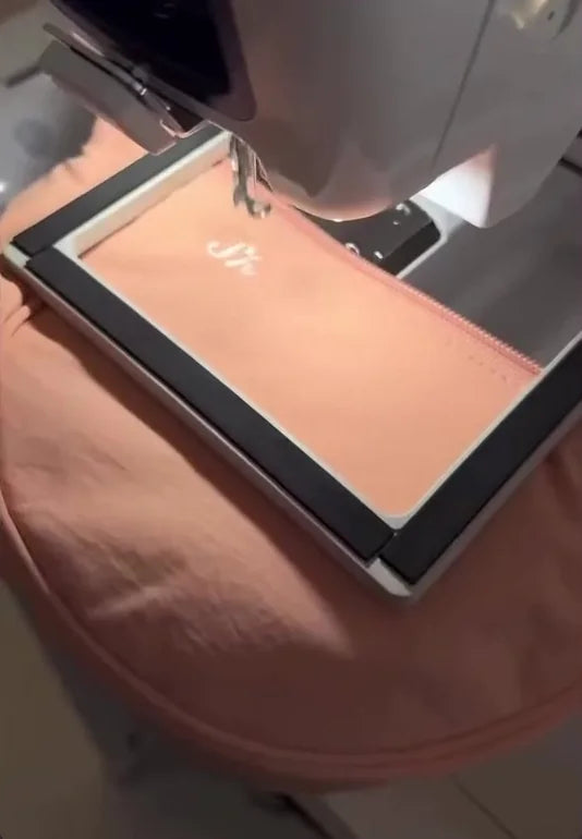 Peach shoulder bag held in a hoop beneath an embroidery machine.