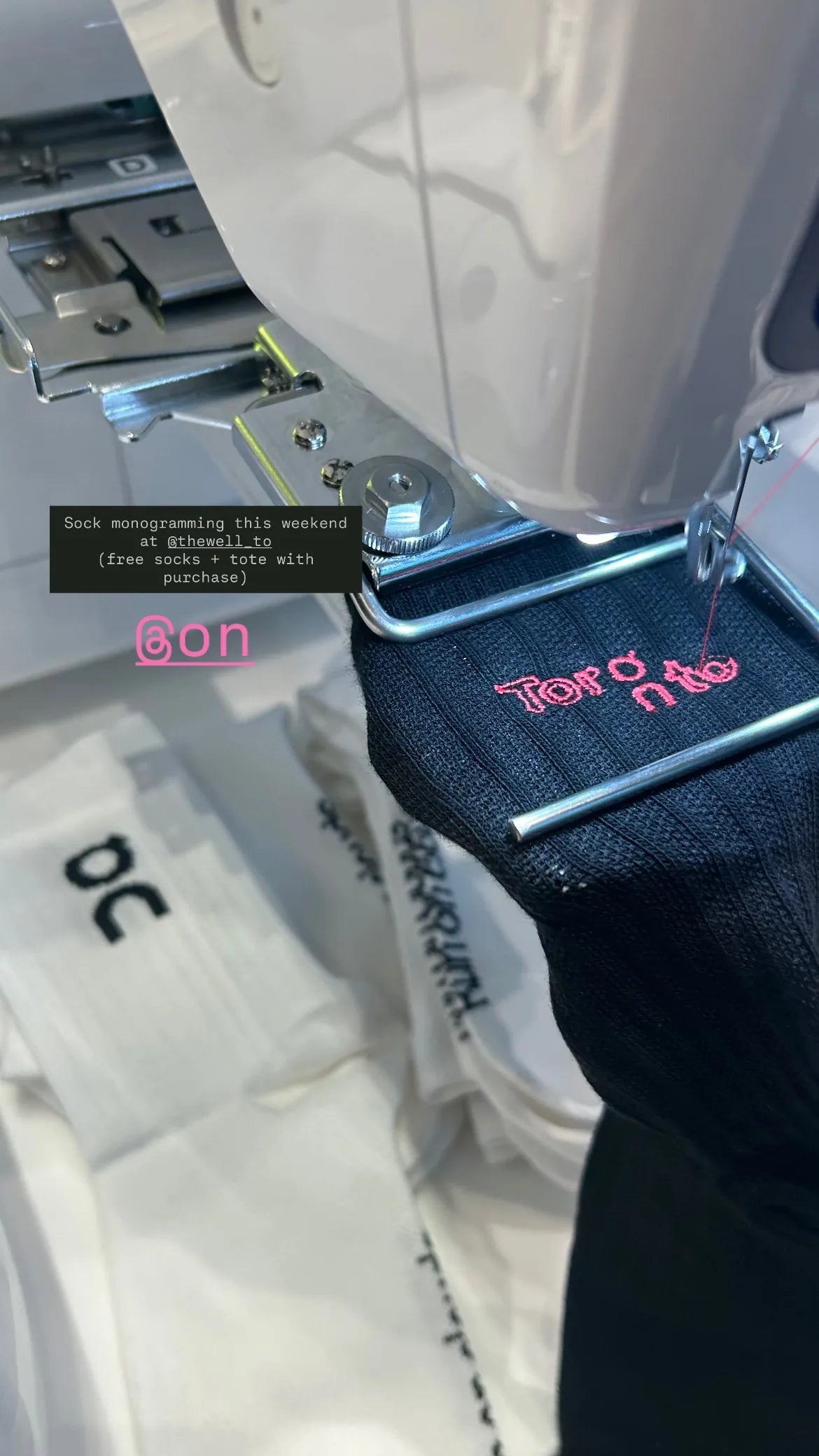 An embroidery machine adding pink lettering to a dark On sock.