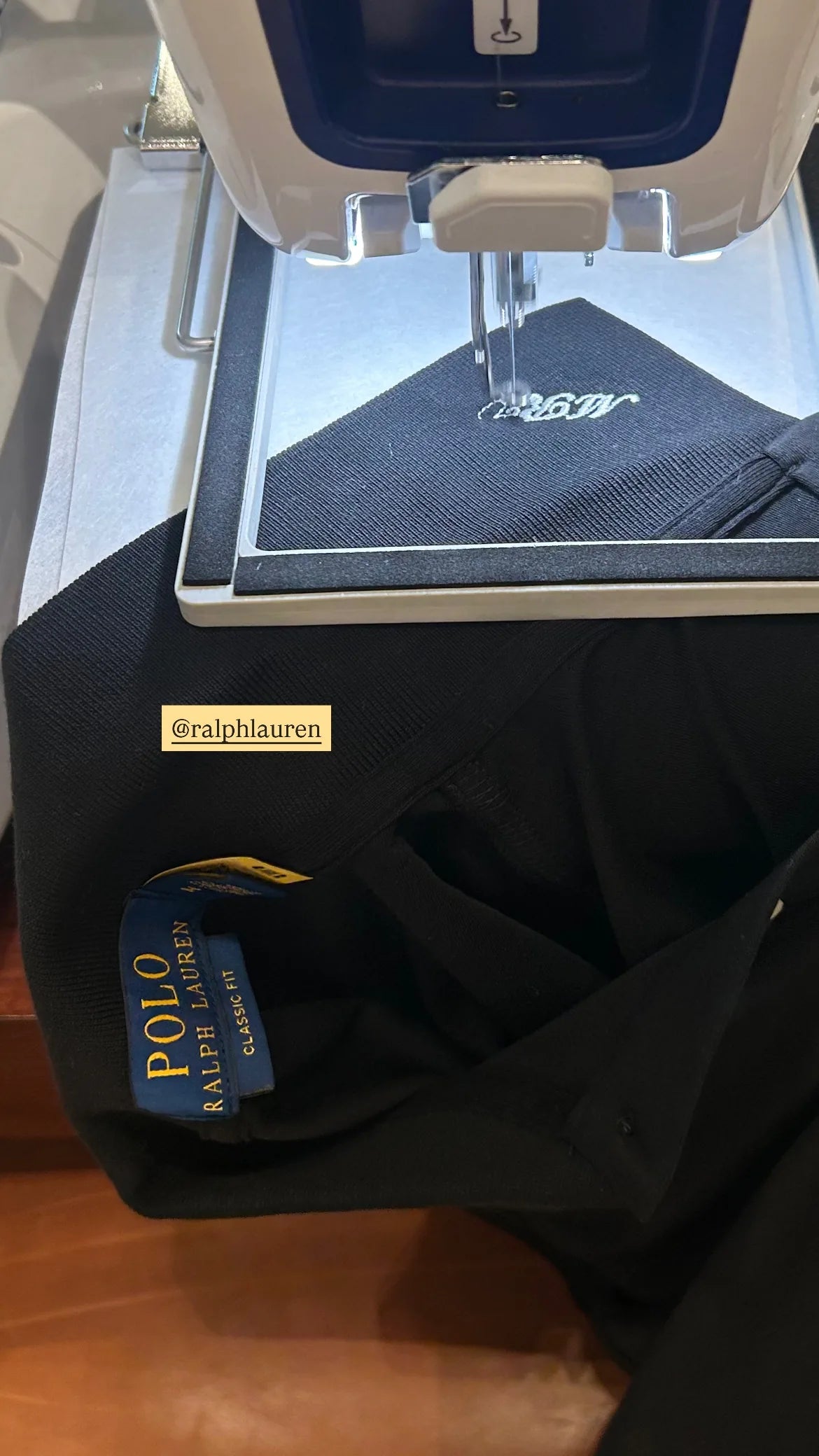 White lettering being embroidered onto a dark Ralph Lauren garment.